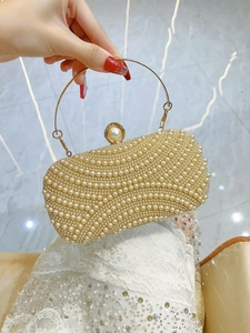 Macro view of champagne pearl evening bag featuring gold metal handle and pearl clasp