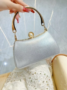 Detail of silver glitter evening clutch featuring a gold metal handle and pearl clasp closure
