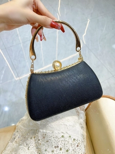 Detail of a black evening clutch with a gold metal handle and a pearl clasp decoration