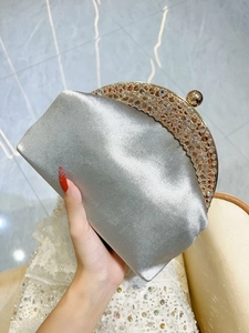Close-up of silver satin evening clutch with gold rhinestone frame and spherical clasp