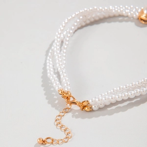 Close-up of golden lobster clasp and adjustable extension chain on layered pearl necklace
