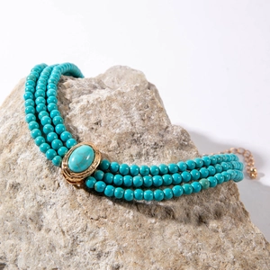 Detailed close-up of three-strand turquoise bead necklace with ornate gold oval pendant