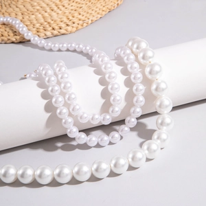 Close-up of layered faux pearl necklaces in different sizes on minimalist props
