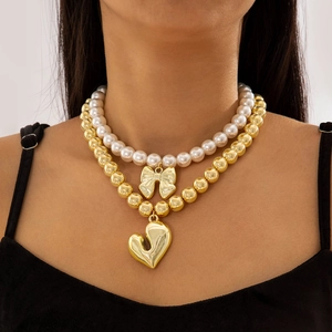 Detalle del collar de capas con cuentas doradas, perlas y colgantes de lazo y corazón