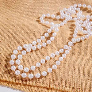 Detailed view of layered white faux pearl necklace on rustic burlap background texture