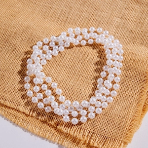Macro detail of triple-layer faux pearl necklace on natural textured brown linen fabric