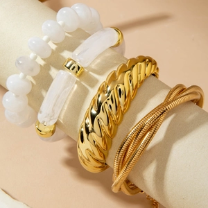 Detail of four-piece gold metal bracelet set with white beads on a warm display stand