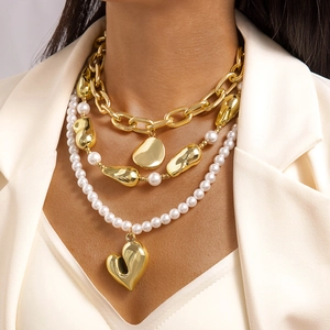 Detalle de collar multicapa de cadena cubana dorada con perlas y colgante de corazón