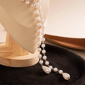 Detail of elegant gold layered necklace featuring round white pearls and teardrop pendants