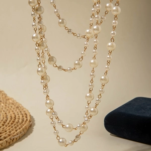 Close-up of multi-layer faux pearl necklace with gold chains on warm beige background