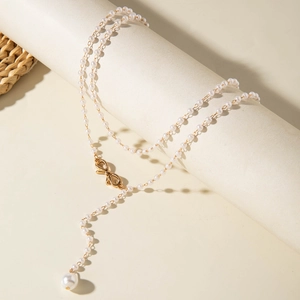 Detailed Y-shaped pearl necklace featuring a gold bow pendant on a jewelry display stand
