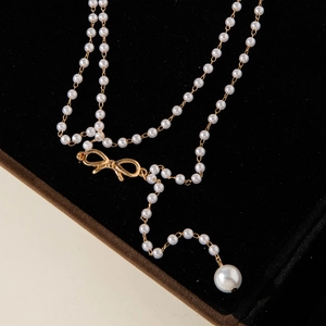 Close-up of pearl necklace featuring a gold bow detail and large teardrop pearl drop