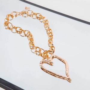 Close-up of chunky gold layered chain necklace with a hammered heart pendant on reflective glass