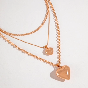 Close-up of layered gold chain necklace featuring polished 3D heart-shaped pendants