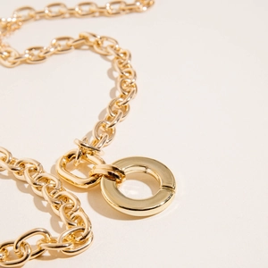 Detailed close-up of chunky gold-tone link chain with large circular geometric clasp