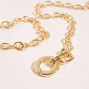Detail of chunky gold chain necklace with large circular fastener on beige background