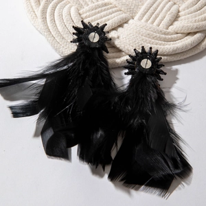 Detail of long black feather earrings featuring ornate beaded flower studs on white texture
