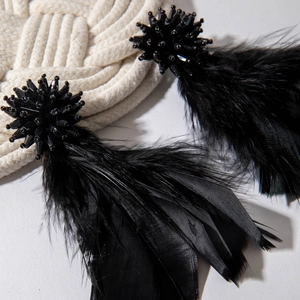 Close-up of elegant black feather earrings with beaded sphere and fluffy texture
