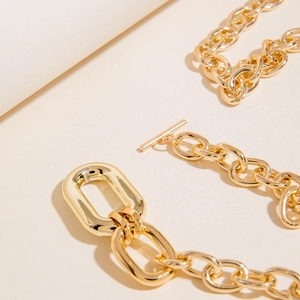 Close-up of polished gold chunky aluminum chain with geometric OT toggle clasp detail