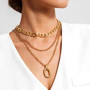 Close-up of layered gold chunky Cuban link necklace with oval pendant on neck