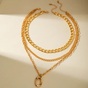 Close-up of layered gold chunky chain necklace with oval pendant and lobster clasp detail