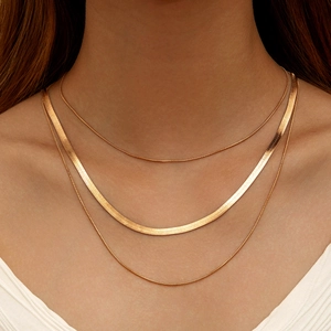 Close-up of layered gold snake chains and textured flat blade necklace on model
