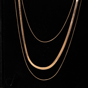 Detailed close-up of triple-layered gold-tone chain necklace set on black velvet background