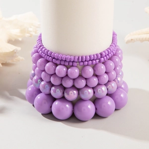 Layered purple resin beaded bracelet set displayed on a white stand with coastal decor