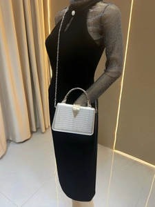 Detailed view of silver evening clutch with wavy texture and gold leaf clasp on a model