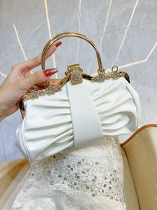 Detail of white pleated evening clutch featuring golden handles and rhinestone flower accents