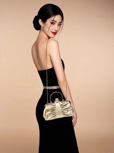 Golden pleated evening clutch bag with metal handle and chain strap held by a model
