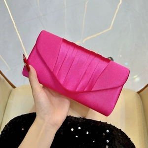 Detail of fuchsia pleated silk satin evening clutch bag held against sequin dress