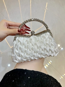 Close-up of white satin evening bag with pleated texture and crystal-embellished handle