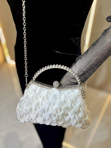 Detail of white satin evening bag featuring rhinestone handles and crystal clasp lock