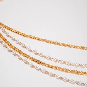 Détail d'une chaîne de taille multicouche avec maillons dorés et perles blanches