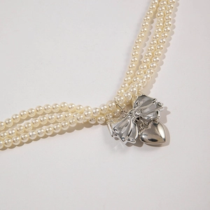 Détail d'un collier de perles à trois rangs avec nœud argenté et pendentif cœur élégant
