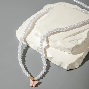 Detail of pink butterfly pendant and white faux pearls on a gold layered body chain