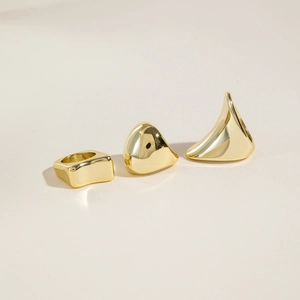 Dettaglio di tre anelli geometrici in oro lucido con forme scultoree minimaliste