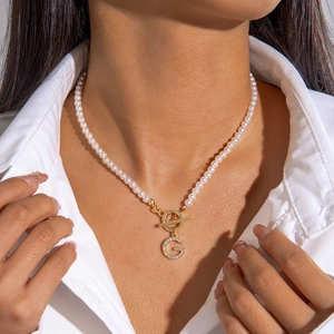 Gros plan du collier de perles avec fermoir OT doré et pendentif lettre G en cristal