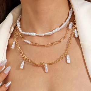Détail du collier multicouche à chaîne trombone dorée et perles baroques sur blazer blanc