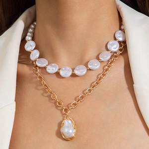Détail d'un collier doré à deux rangs avec perle baroque sur un blazer blanc