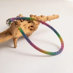 Close-up of rainbow rhinestone choker necklace draped on organic wooden display
