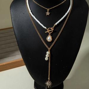 Détail d'un collier doré multicouche avec fermoir OT, perles et pendentifs en étoile