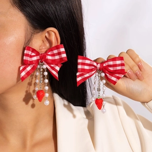 Détail de boucles d'oreilles à nœud écossais rouge avec perles et pendentifs fraises