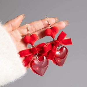 Close-up of red velvet bow and resin heart drop earrings held by hand