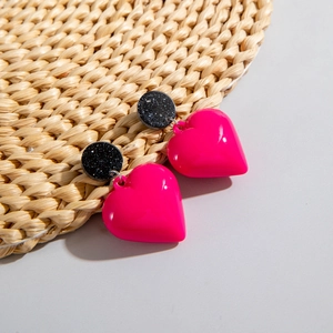 Close-up of heart-shaped acrylic earrings in pink and black glitter finish on a woven mat
