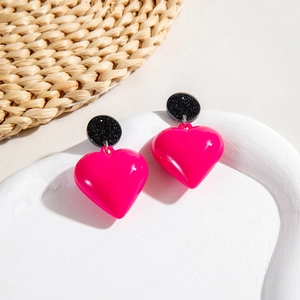 Detail of hot pink heart drop earrings with black glitter studs on a white tray