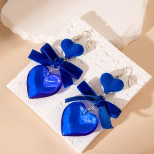 Detail of blue velvet bow and heart earrings on a natural stone surface for display