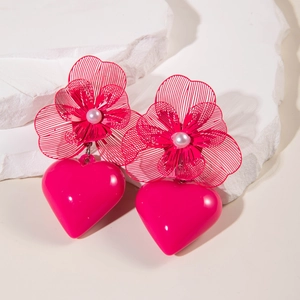 Close-up of bright pink heart drop earrings with metal floral detail and white pearl