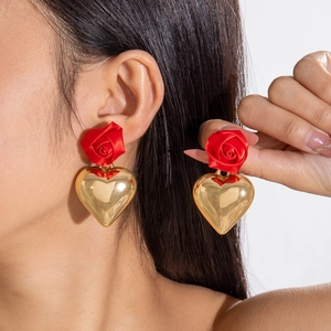 Detailed view of vintage red rose and golden heart earrings worn for a romantic style
